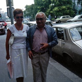 Older couple stands near a car on a city street.