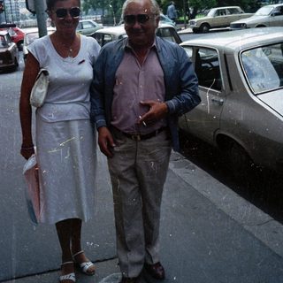 Older couple stands near a car on a city street.