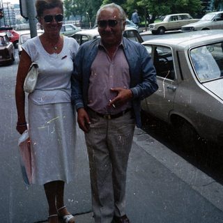 Older couple stands near a car on a city street.
