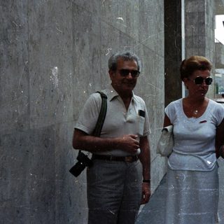 Three people standing on a street near a wall.