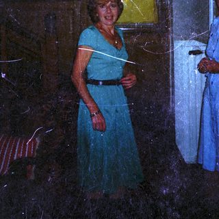 Here's a brief summary of the image: Woman in dress stands near a window and person.