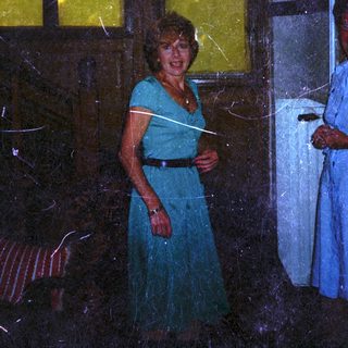 Here's a brief summary of the image: Woman in dress stands near a window and person.