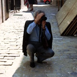 Man takes a photo in a narrow, cobbled alleyway.