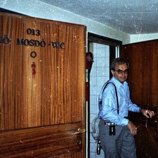 Man stands in a hallway near a restroom door.
