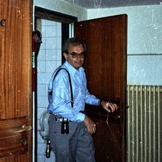 Man stands in a hallway near a restroom door.