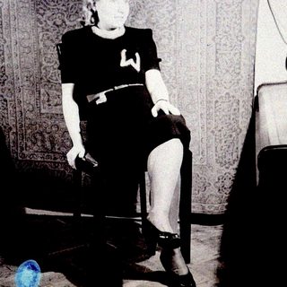 Here's a brief summary of the image: Woman seated in a chair, wearing a dress and heels.