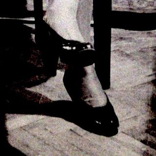 Here's a brief summary of the image: Woman seated in a chair, wearing a dress and heels.