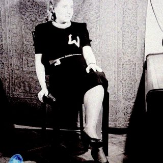 Here's a brief summary of the image: Woman seated in a chair, wearing a dress and heels.