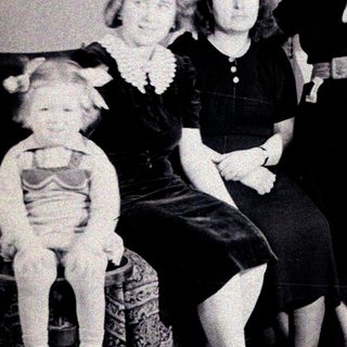 Three women and a child pose indoors, vintage clothing.