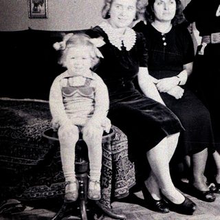 Three women and a child pose indoors, vintage clothing.
