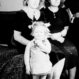 Here's a brief summary of the image: A young girl stands with two women in a home.