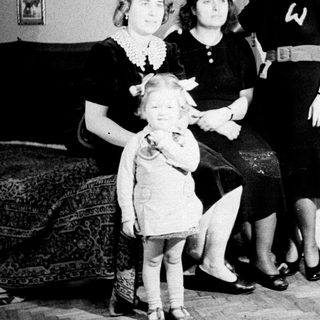 Here's a brief summary of the image: A young girl stands with two women in a home.