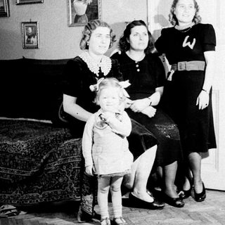 Here's a brief summary of the image: A young girl stands with two women in a home.