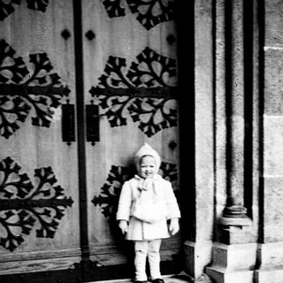 Child in a coat stands before a carved door.