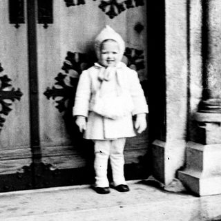 Child in a coat stands before a carved door.