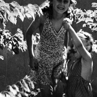 Two children are playing outdoors amongst foliage and greenery.