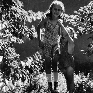 Two children are playing outdoors amongst foliage and greenery.