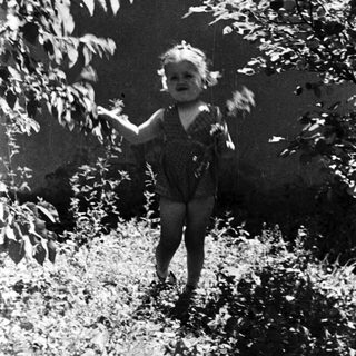 Child playing outdoors, surrounded by foliage and greenery.