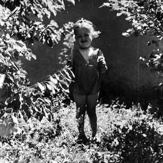 Here's a brief summary of the image: Young child stands in foliage, captured in a vintage photograph.