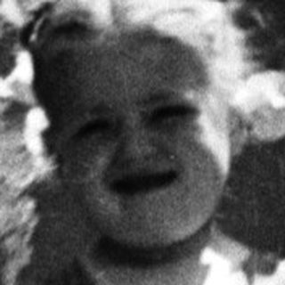 Here's a brief summary of the image: Young child stands in foliage, captured in a vintage photograph.
