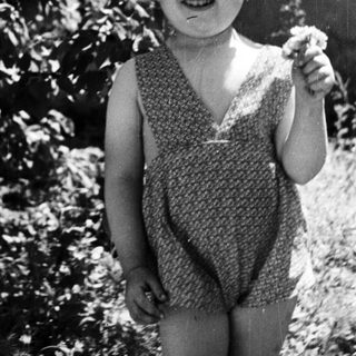 Girl smiles, stands near tree in vintage black and white photo.