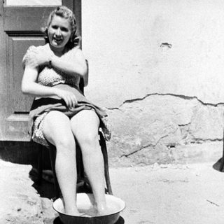 Woman sits, soaking feet in a bowl outdoors.