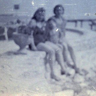 Faded, monochrome image of two people near a fence.