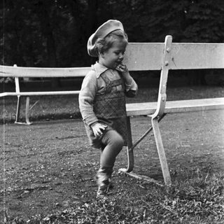 Here's a brief summary of the image: Young child stands near a bench in a grassy area.