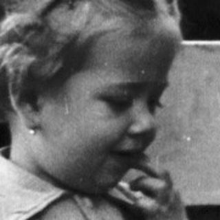 Here's a brief summary of the image: Young child stands near a bench in a grassy area.