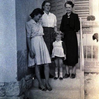 Three women and a young girl stand outside a building.