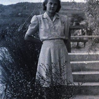 Woman stands on stone steps under a tree.