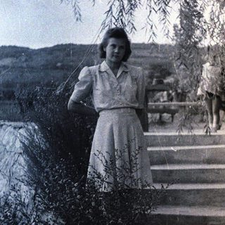 Woman stands on stone steps under a tree.