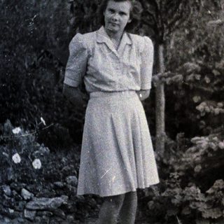 Woman stands in a garden, posed near foliage.