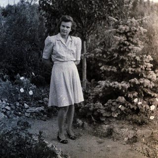 Woman stands in a garden, posed near foliage.