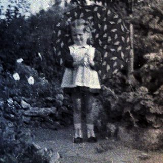 Girl stands near trees in a vintage black and white photo.