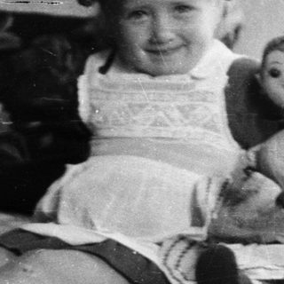 Girl with a doll sits on a bed.