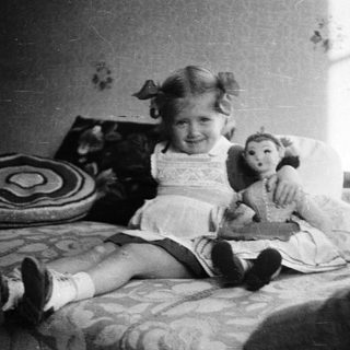 Girl with a doll sits on a bed.