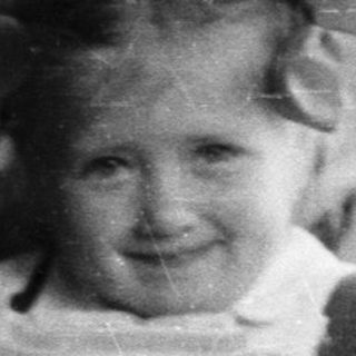 Girl with a doll sits on a bed.