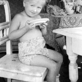 Here's a brief summary of the image: Young girl sits, holding a plate at a table.