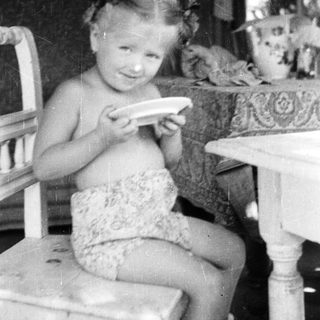 Here's a brief summary of the image: Young girl sits, holding a plate at a table.