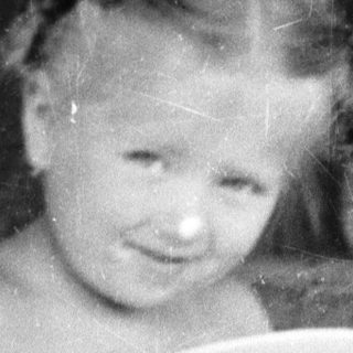 Here's a brief summary of the image: Young girl sits, holding a plate at a table.