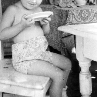 Here's a brief summary of the image: Young girl sits, holding a plate at a table.