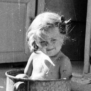 Baby sitting in a bucket outdoors.