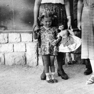 Girl with doll stands with three women outside a house.