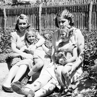 Three young women sitting outdoors in a garden scene.