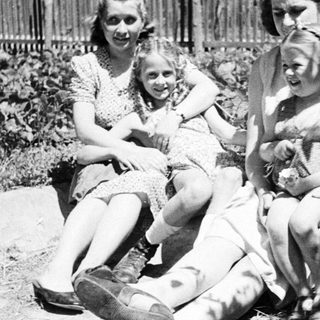 Three young women sitting outdoors in a garden scene.