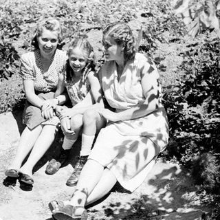 Three women sit outdoors, appearing to be in a garden.