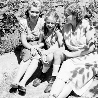 Three women sit outdoors, appearing to be in a garden.