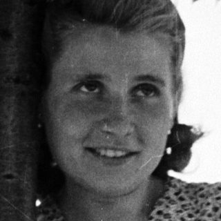 Woman stands smiling near a tree, in a vintage photograph.