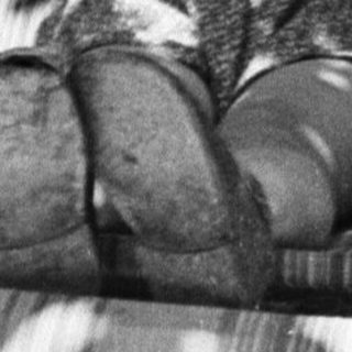 Here's a brief summary of the image: Child sits in a chair, hands behind head, smiling.